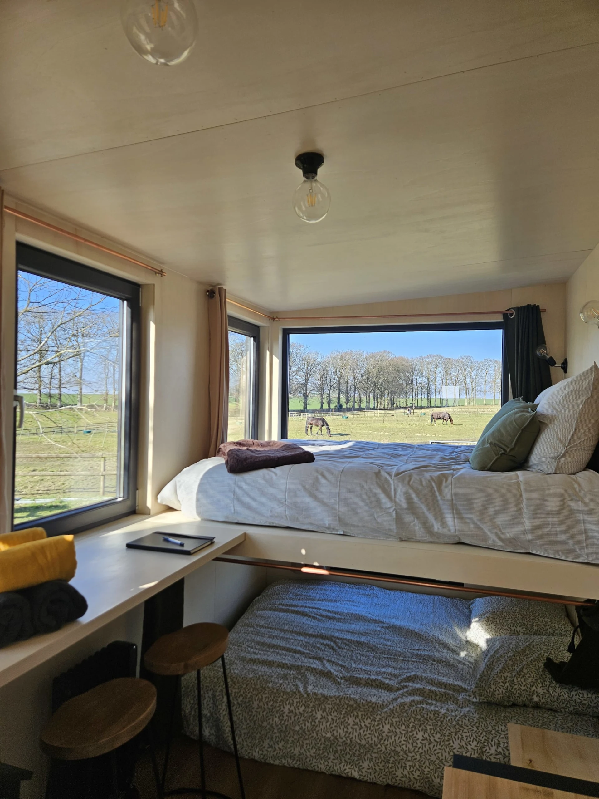Lit principal de la tiny house avec vu sur les chevaux et la nature