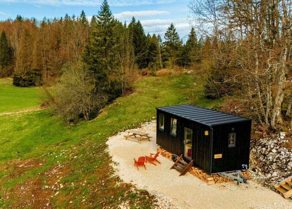 Tiny House L'Alpage au milieu de la forêt des montagne avec un ciel bleu des sapin vert et une terrasse extérieure